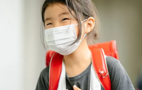 little girl wearing a backpack and a mask smiling with her eyes