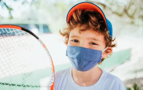 boy holding a tennis racket wearing a mask