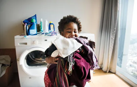 girl with an armful of laundry with the washer dryer in the background