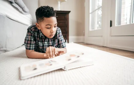 Young boy reads a book while lounging on the floor