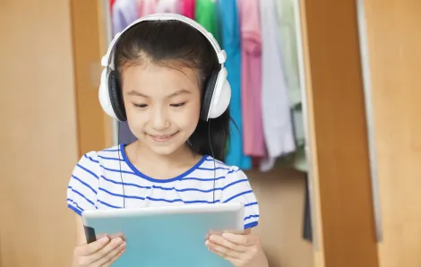 Young girl wearing headphones and viewing content on a tablet computer