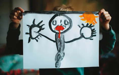 kid holding up a drawing of a black figure with red lips and a yellow sun in the background