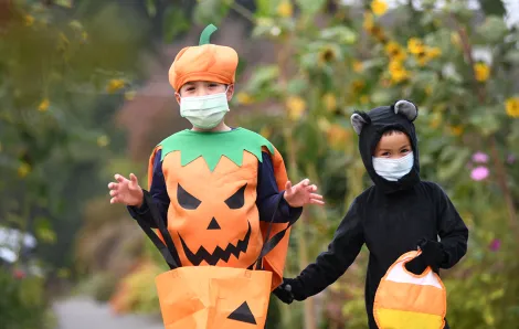boys wearing a pumpkin and cat costume and face masks for Halloween 2020