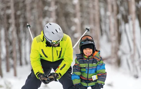 black father and son bundled up standing side by side in the snow ready to ski