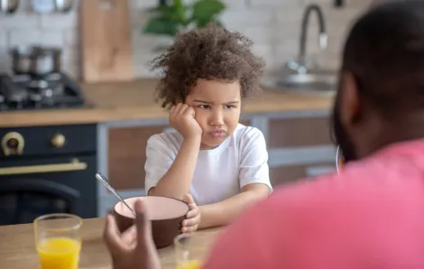 kid frowning over a bowl at the kitchen table