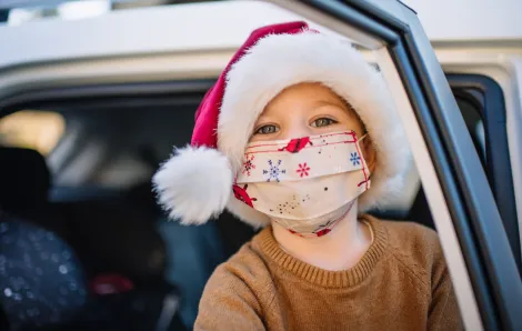 Little boy wearing protective face mask and Santa hat in car on Christmas