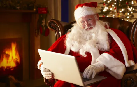 santa sitting in front of a fire holding a laptop