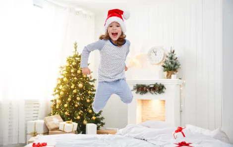 girl wearing a santa hat jumping on the bed