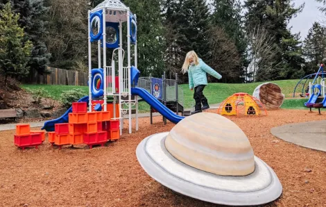 Child climbing on planet-shaped play feature at new space-themed playground now open at North Kirkland Community Center
