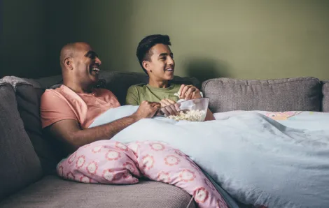 father and teen son under a blanket on the couch watching a movie