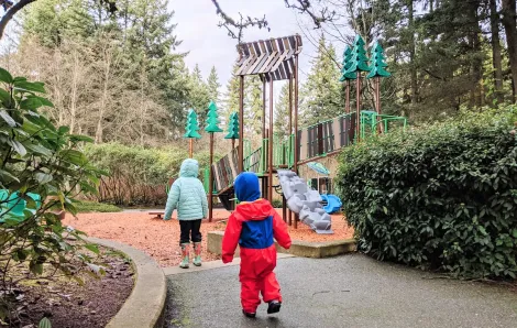 Young kids dressed for rainy weather approaching a new playground at Heron Park in Mill Creek, a small city near Seattle Washington