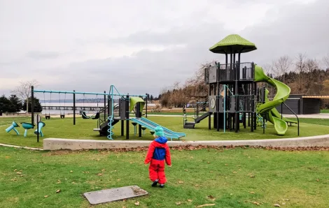 Small boy in red rain suit looking at new playground equipment installed at Kirkland's Juanita Beach Park near Seattle