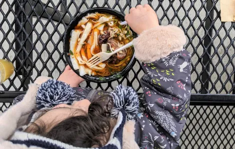 Young girl in flowered jacket eats ox tail noodle soup from Spice Bridge Food Hall in Tukwila Washington near Seattle