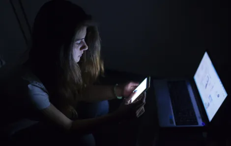 teenage girl in the dark with her laptop and phone screens lit up