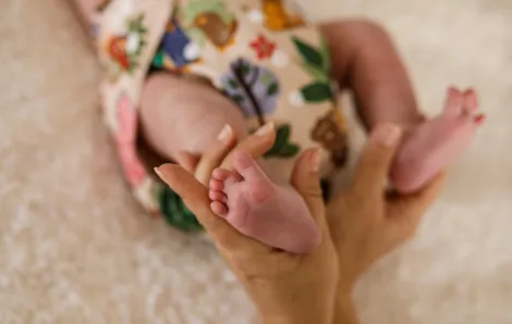 closeup of a baby's cloth diaper with cartoon leaves and a mother's hand holding onto the baby's leg