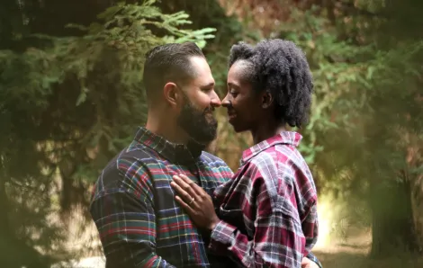 interracial couple with their noses together with pine trees in the background