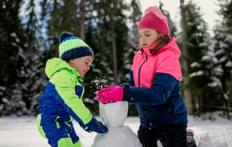 Brother and sister about ages 6 and 8 wearing snowsuits together build a snowman at new Seattle-area Sno-Park at Lake Easton along Interstate 90