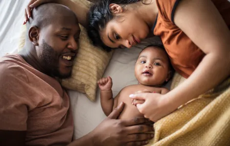 parents with their baby laying in bed with all three smiling