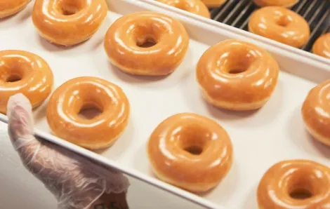 Gloved hand holding a tray of Krispy Kreme glazed doughnuts free doughnut a day for the year for vaccinated individuals