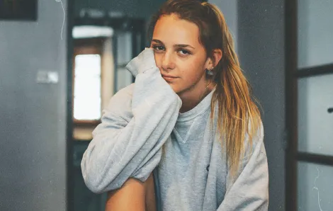 Teenage girl in a sweatshirt rests her head on her hand