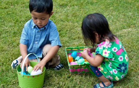Two small kids brother and sister sitting in the grass and inspecting their Easter baskets full of plastic eggs