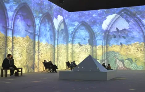 People in chairs watching Van Gogh The Immersive Experience video projections on the walls around them
