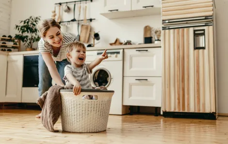 mom pushing her smiling son across the floor in a laundry basket