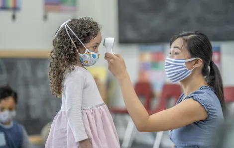 daycare woman in a mask taking a child's temperature