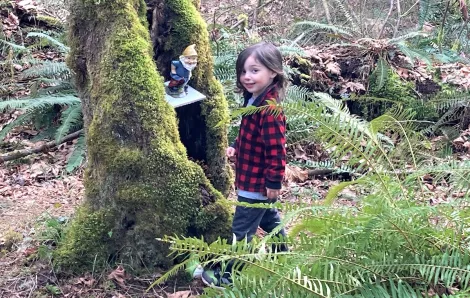 Kid in plaid jacket standing by gnome in tree along Maple Valley gnome trail fun for Seattle-area families