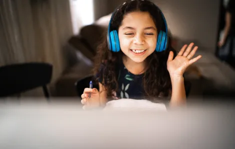 girl wearing headphones waving at her computer