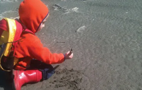 Boy in a red hooded jacket discovers a seashell at the beach