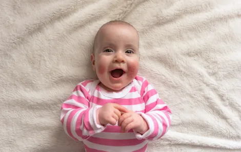 happy smiling baby with red cheeks on a blanket 