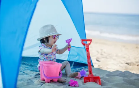 Kid-wearing-sunhat-sitting-in-tent-by-the-beach, sun protection for kids