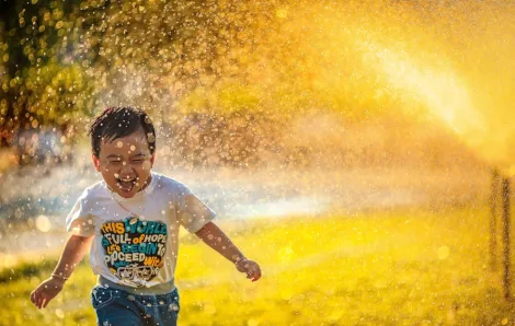 boy running through a sprinkler backlit by the sun