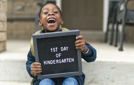happy boy holding a 'first day of kindergarten' sign