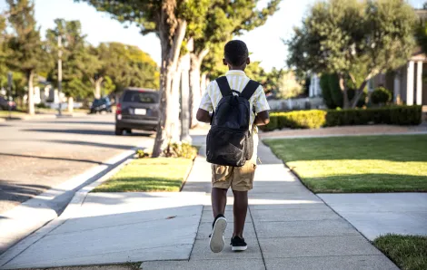 boy wearing a backpack walking alone down a residential sidewalk