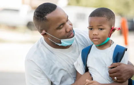 Father consoles anxious kindergartener while they wear masks as he's dropping him off for first day of school