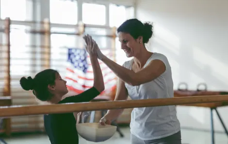 Cute little girl practicing gymnastics and giving her coach a high-five