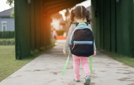 little girl in a backpack walking into school by herself