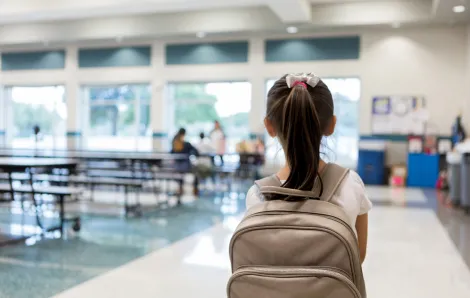 rear view of a girl with a backpack entering a relatively empty school cafeteria