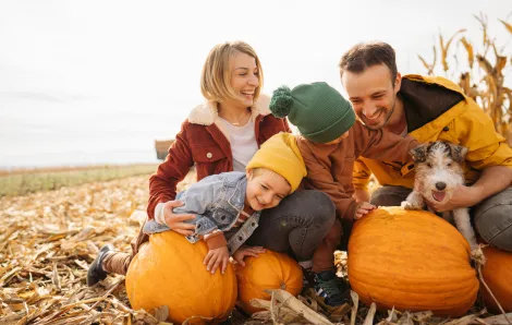 laughing family of four crouched on straw with some pumpkins and a dog