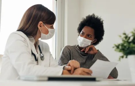 female doctor talking to female patient both wearing masks