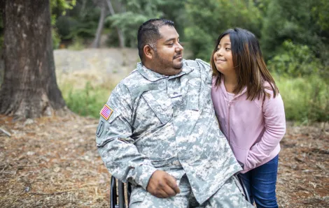 Veteran dad in army fatigues and sitting in wheelchair smiles at and hugs daughter of about age 11. she is smiling at him. veterans day events for families Seattle Bellevue Tacoma Puget Sound