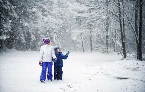 Brother and sister walking in snowy forest 