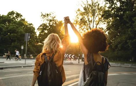 Two young women -- one Black and one white -- walk together, holding each other's hand up high