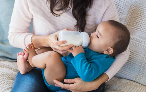 Baby drinking milk from bottle on his nanny's lap