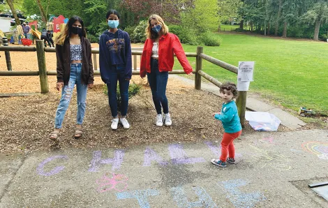 Adults and a child at a park drawing with sidewalk chalk