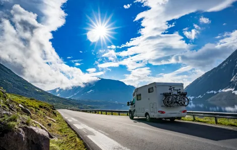 A small RV drives on a road past a lake with mountains in the background sun and clouds in blue sky best family road trip routes itineraries from seattle