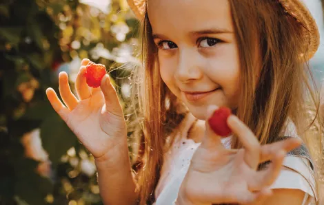 Girl wearing a hat picking raspberries 