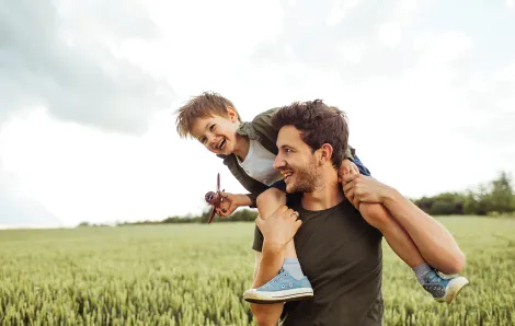 Dad with child on his shoulders in a grass field